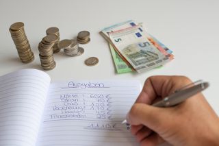 © Sarah - stock.adobe.com Foto: Person schreibt in Haushaltsbuch